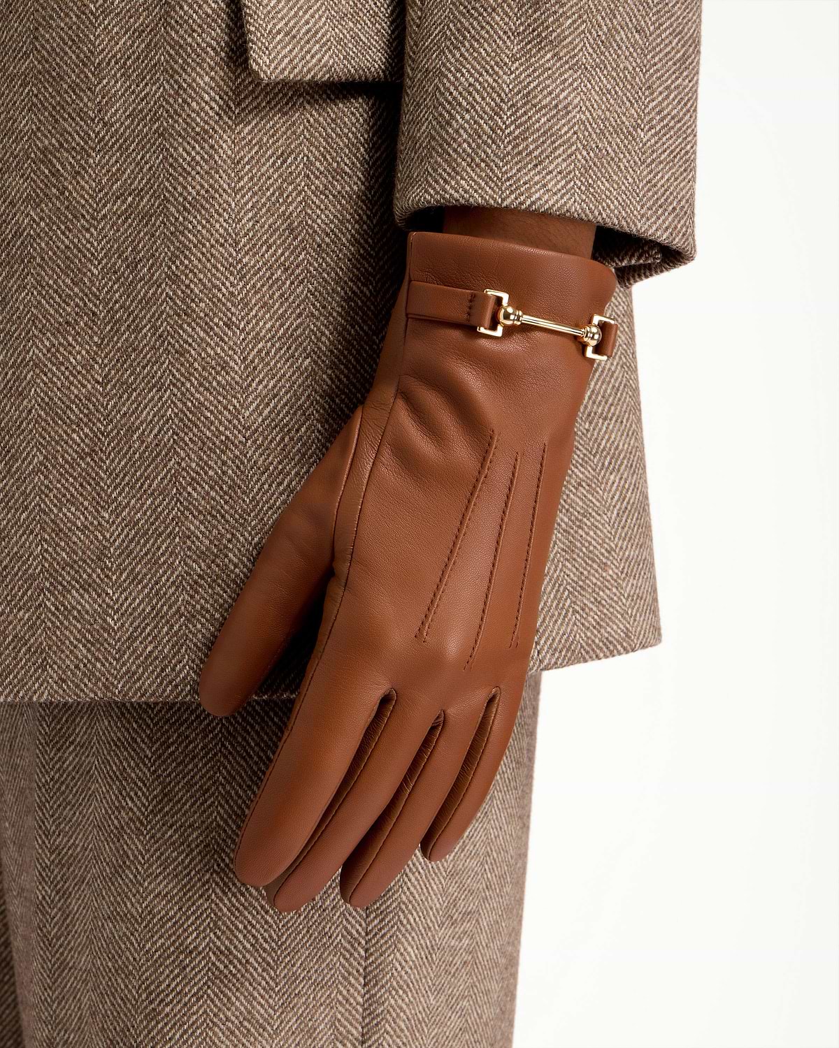 Tan leather gloves with gold bit detail worn with herringbone coat.