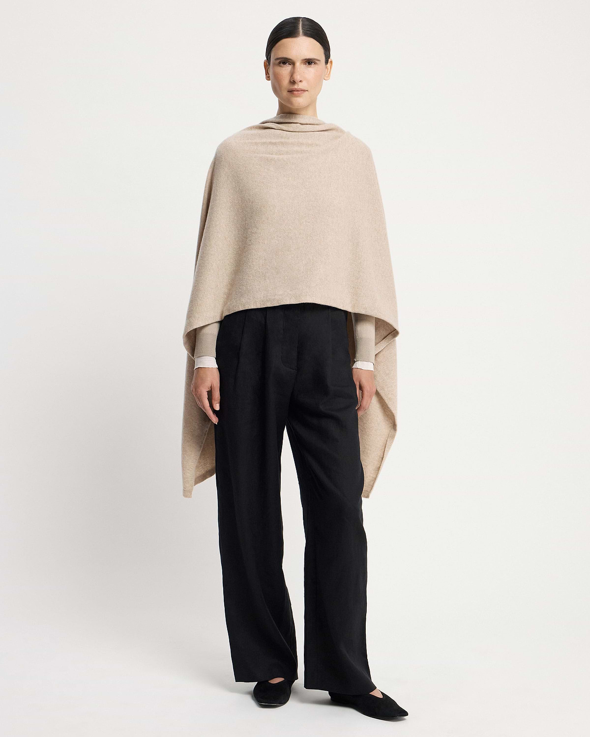 Model wearing an oat cashmere travel wrap draped over shoulders and black trousers