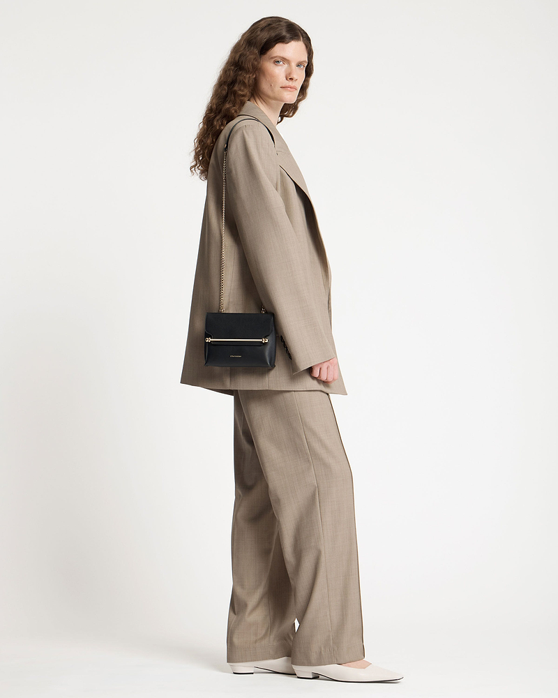 Model wearing a beige suit with a black Strathberry Stylist Mini shoulder bag.