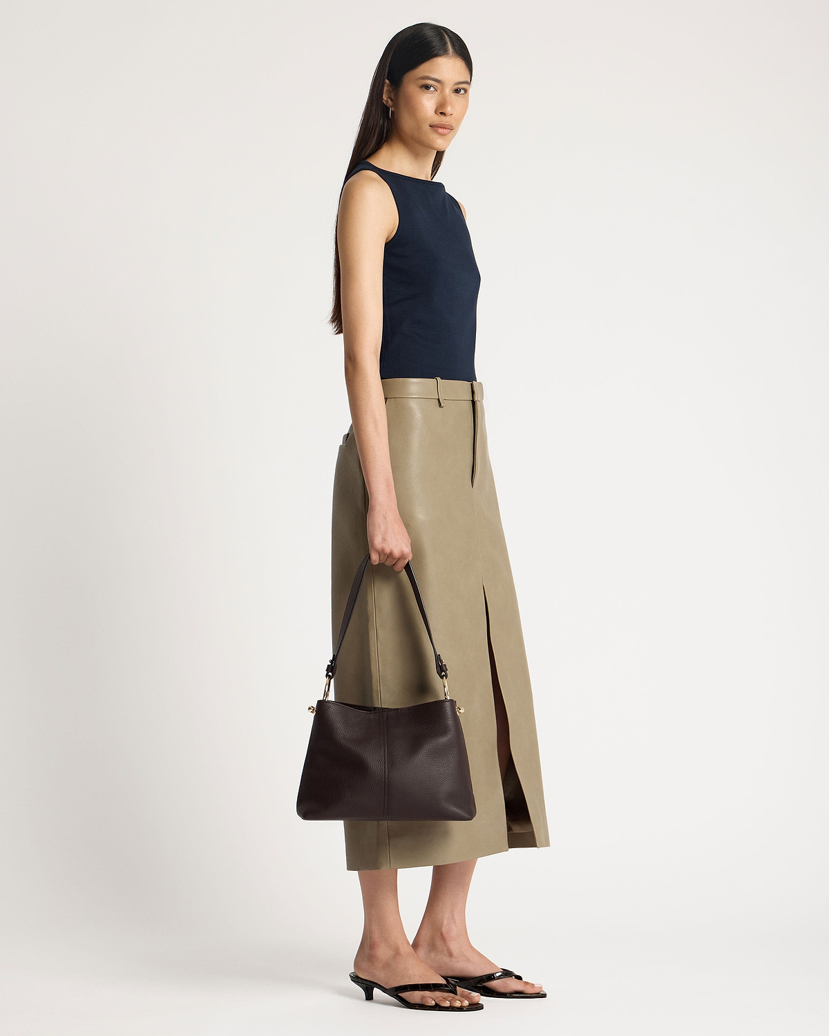 Model holding espresso leather hobo bag at her side, strap and hardware visible.