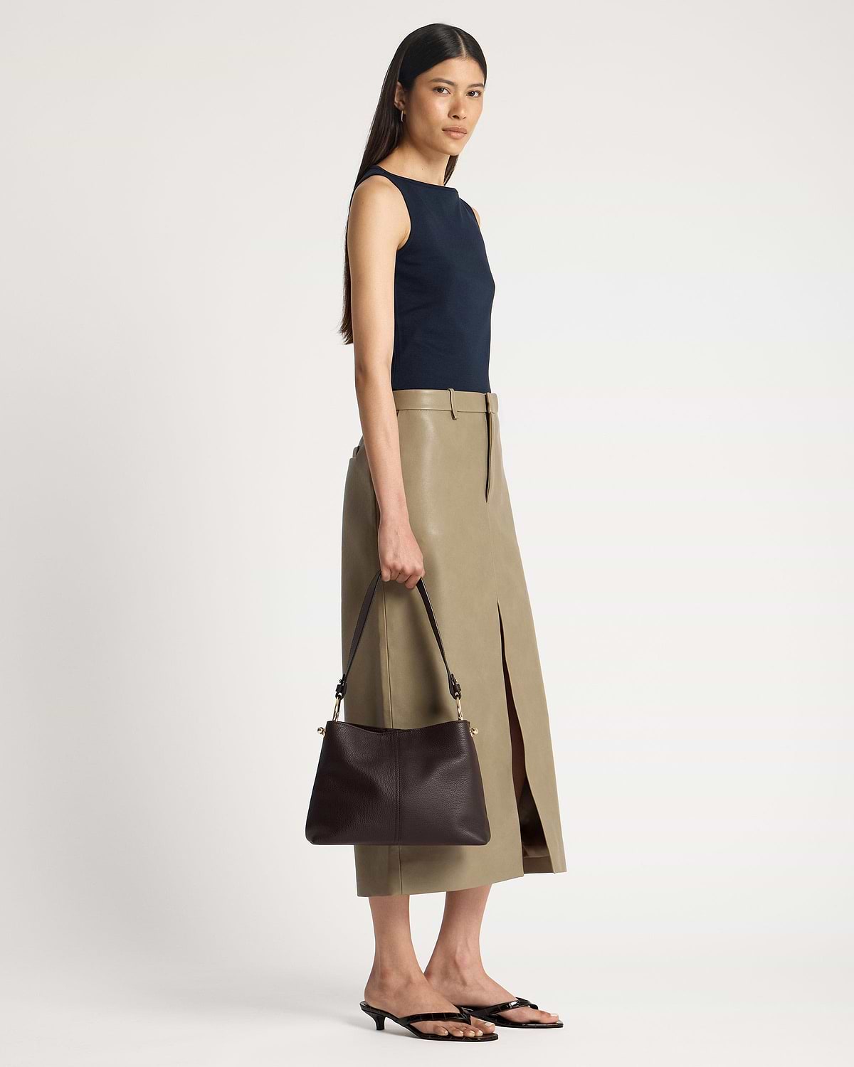 Model holding espresso leather hobo bag at her side, strap and hardware visible.