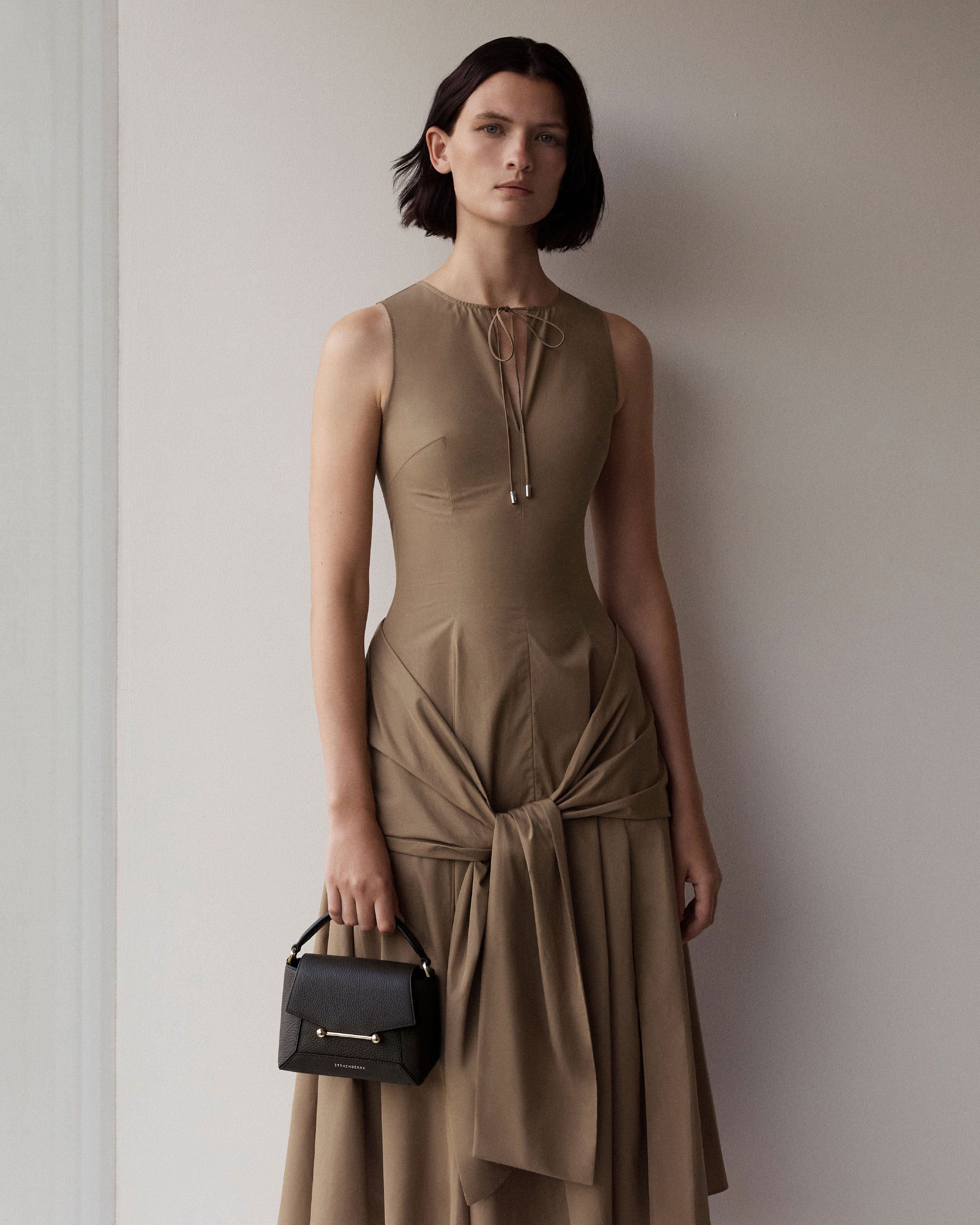 Model holding espresso Mosaic Nano bag by its top handle, Strathberry logo visible.
