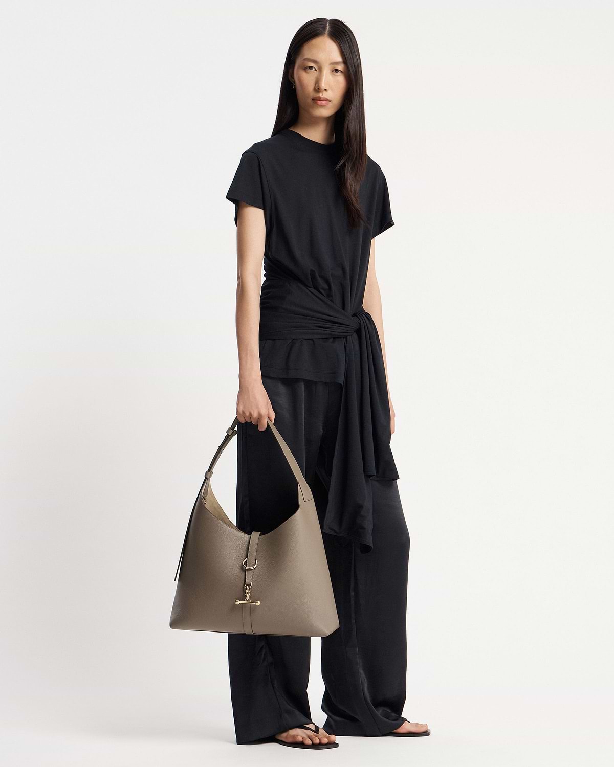 Model in a black outfit holding a taupe hobo bag with gold hardware.