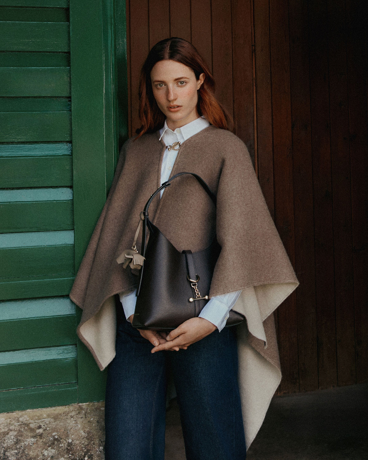 Woman wearing a cape holding an espresso leather Kite Hobo bag with tassel charm
