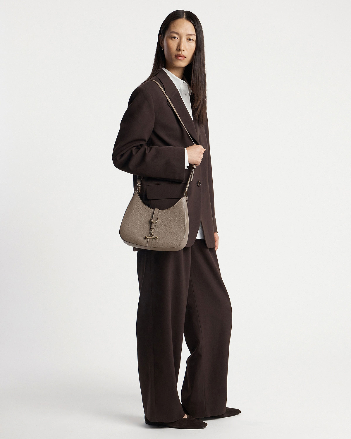 Model wearing a taupe kite sling bag over her shoulder, full body visible.