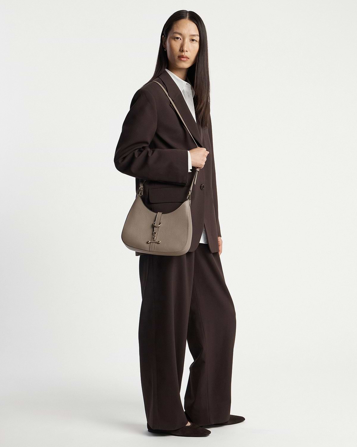 Model wearing a taupe kite sling bag over her shoulder, full body visible.