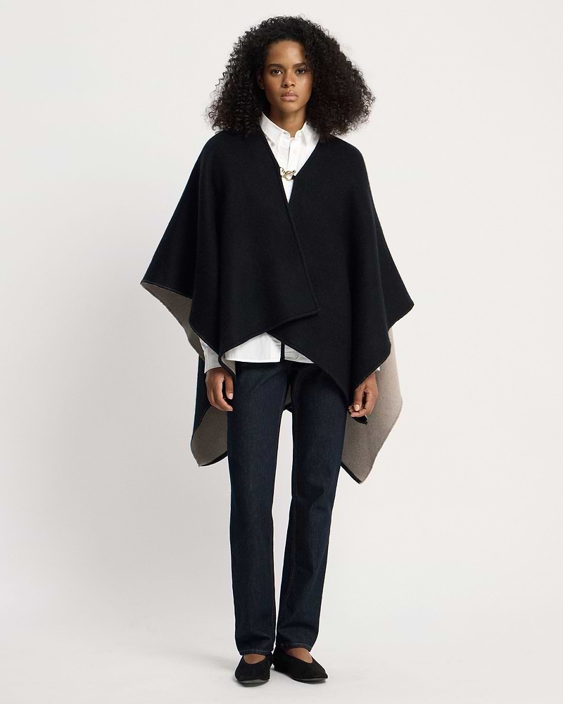 Woman wearing otter and black woven kite cape over white shirt and jeans.