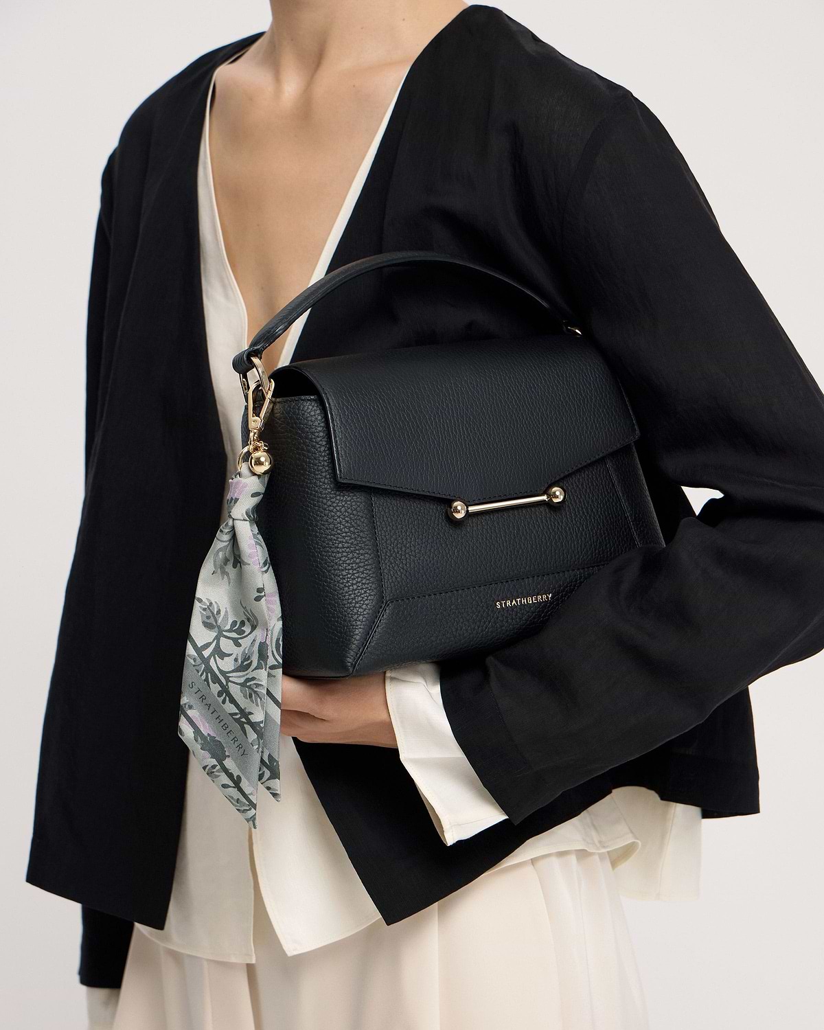 Model waist-up holding black Strathberry leather bag with green thistle-print silk charm.