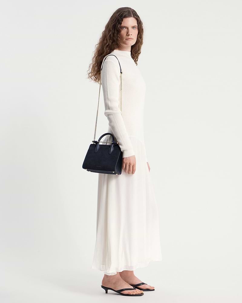 Woman in cream dress carrying navy suede mini tote with gold chain strap.