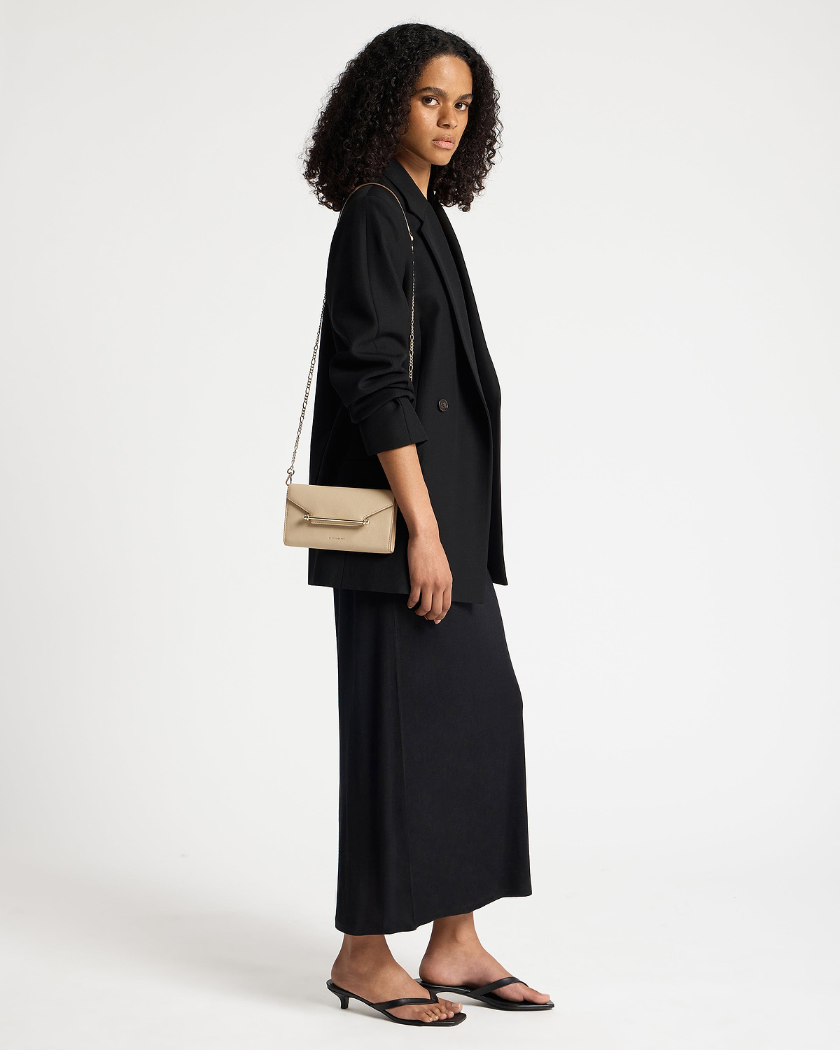 Model wearing sand leather chain wallet with gold chain strap over black blazer.