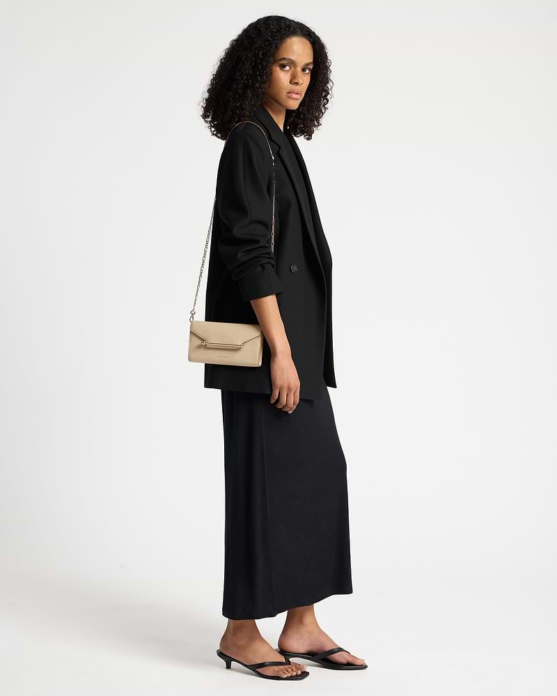 Model wearing sand leather chain wallet with gold chain strap over black blazer.