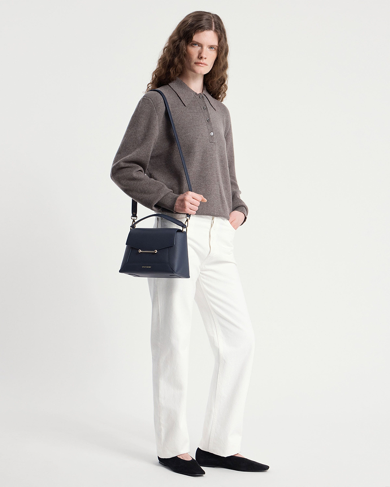 Model wearing grey sweater and white trousers holding navy Strathberry mosaic bag