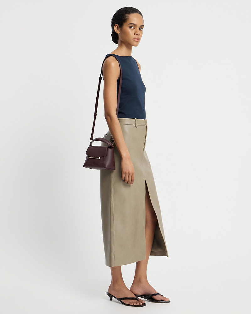 Model wearing navy top and beige skirt carrying burgundy Mosaic Nano bag with shoulder strap