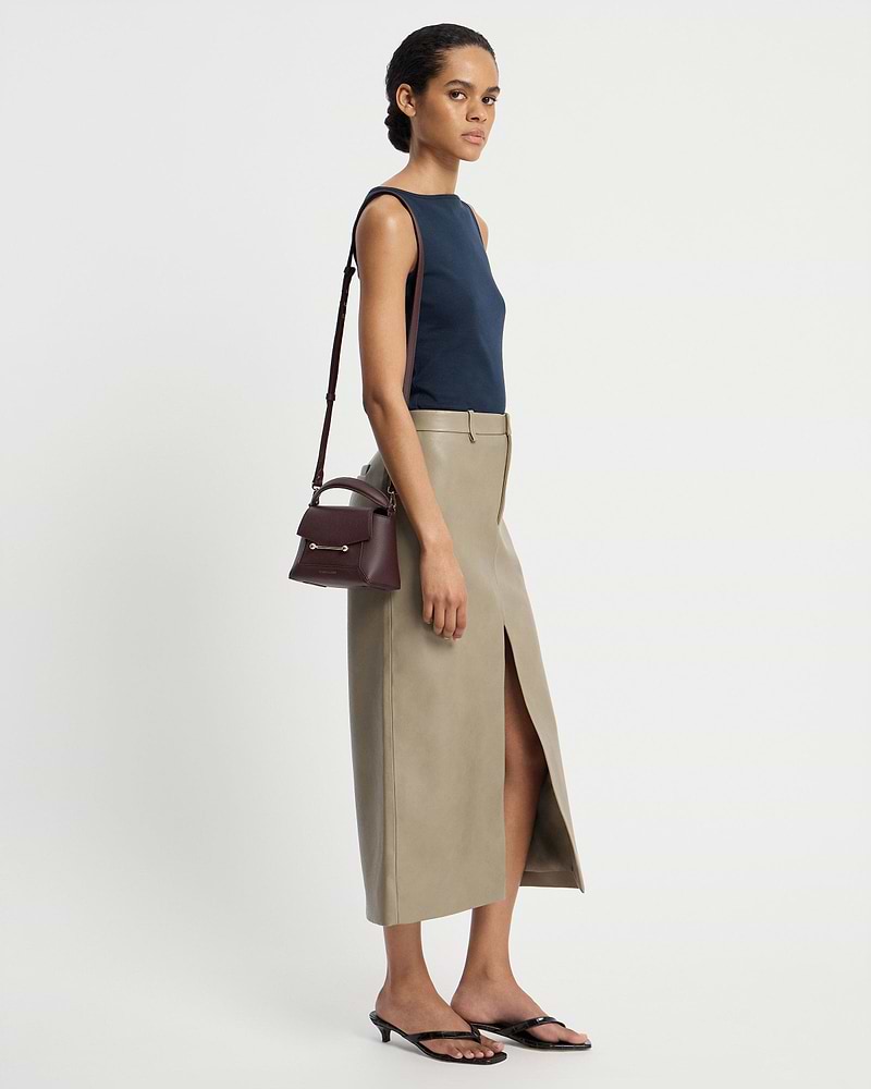 Model wearing navy top and beige skirt carrying burgundy Mosaic Nano bag with shoulder strap