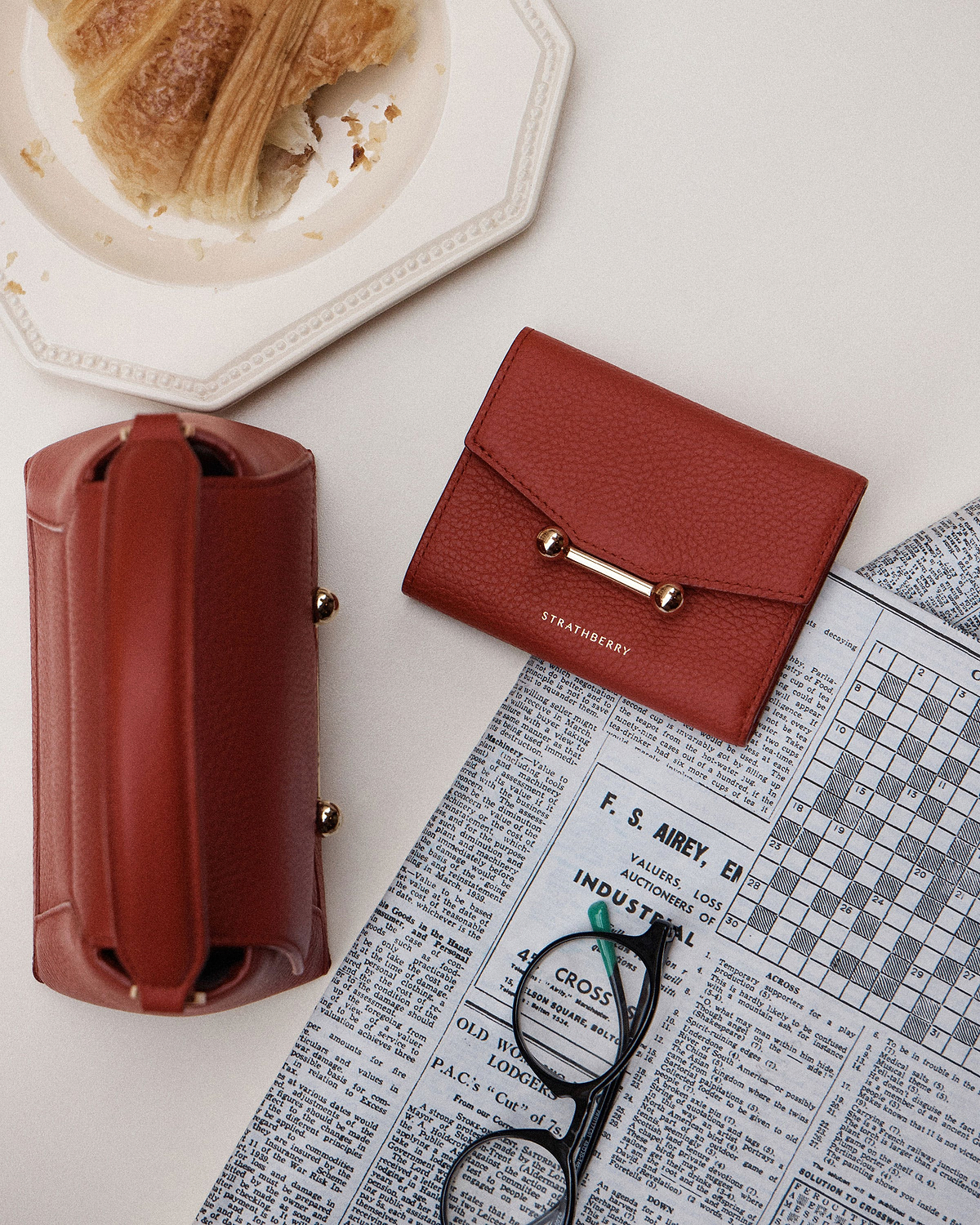 Levanto red mosaic trifold wallet by Strathberry with leather pouch, glasses and croissant.