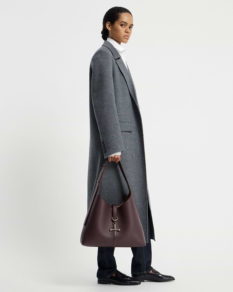 Model holding burgundy leather hobo bag with gold hardware, side view.