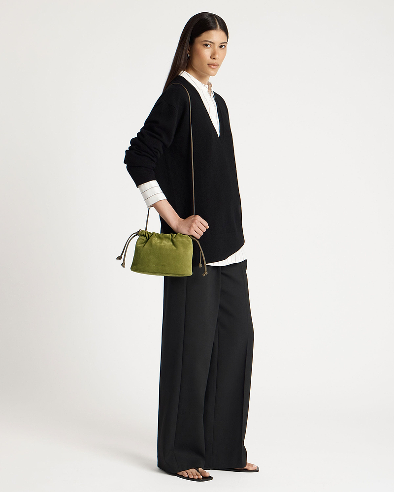 Model wearing black V-neck sweater holds lime suede drawstring bag at her hip.