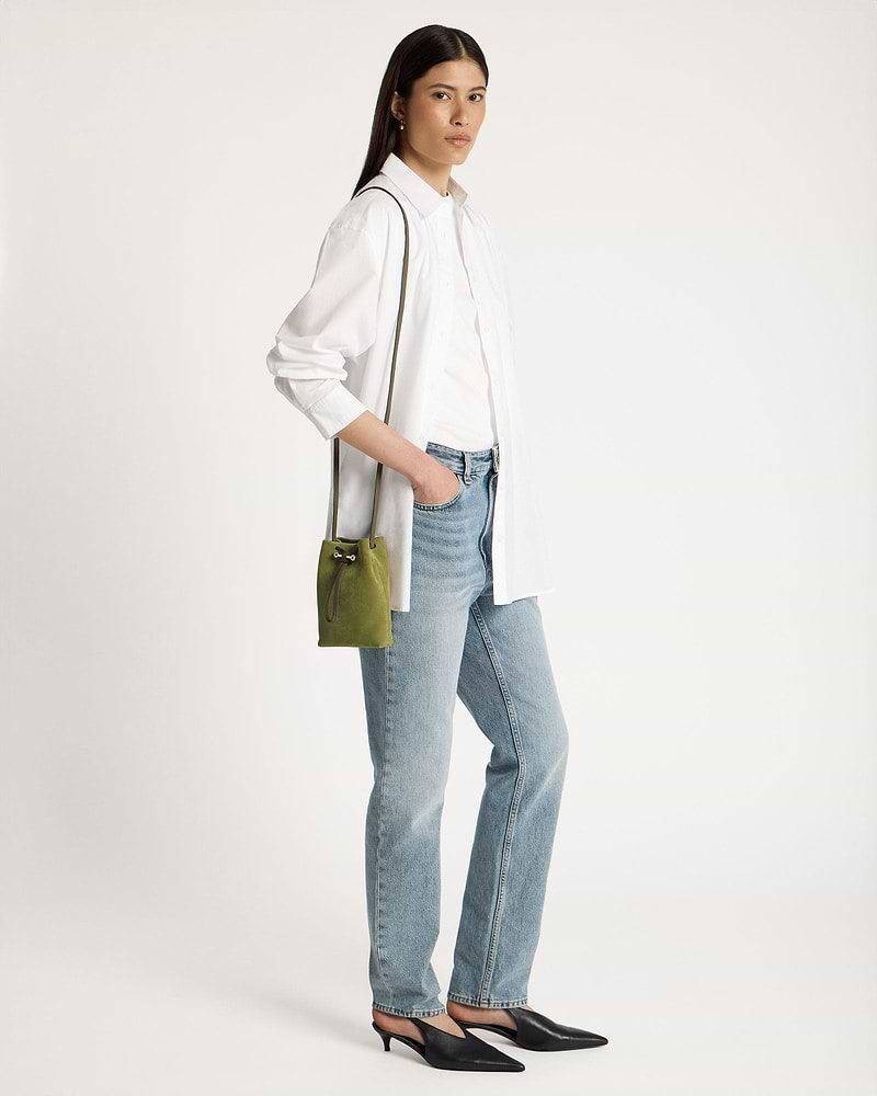 Model wearing white shirt and jeans carrying lime suede and khaki drawstring pouch.