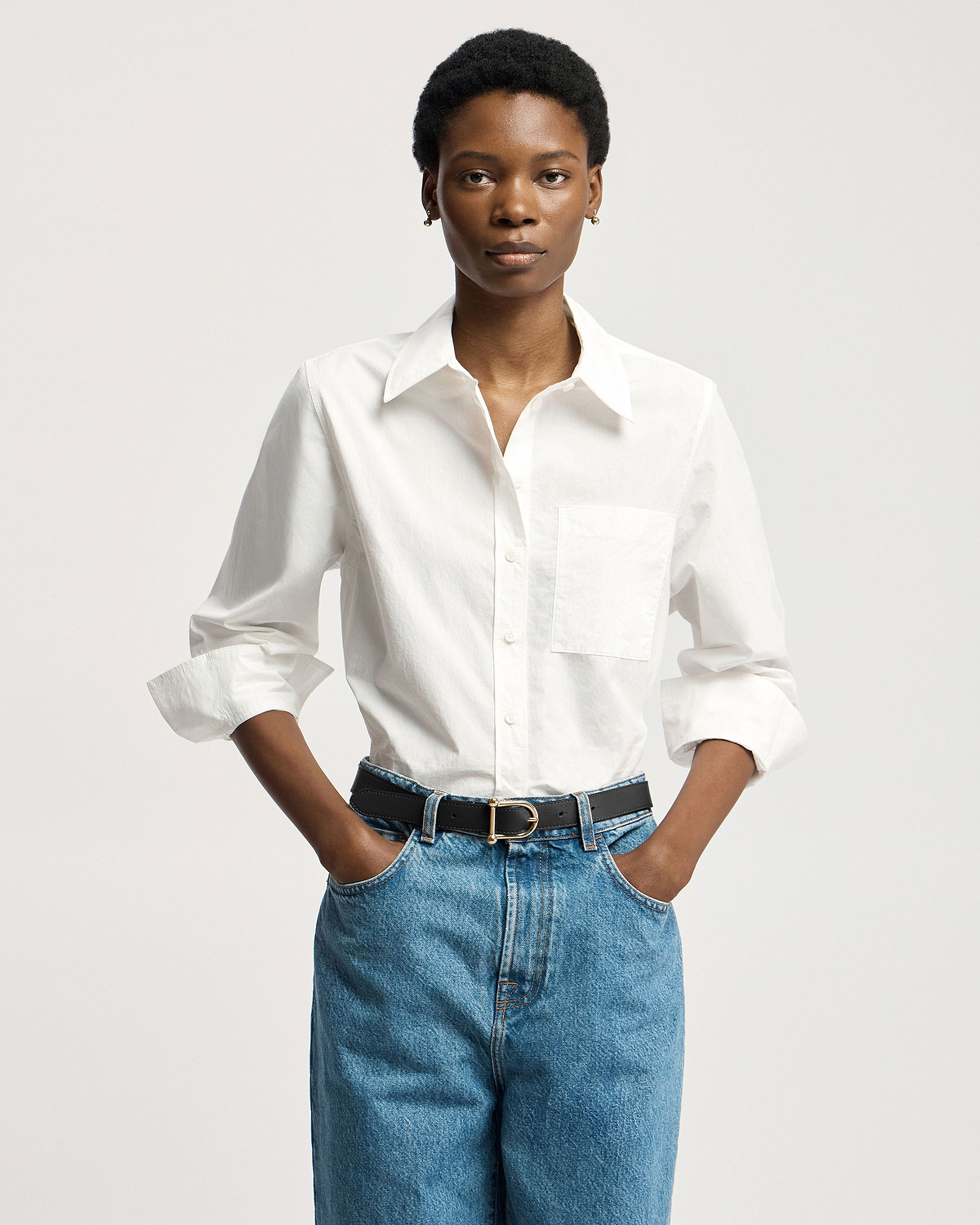 Model wearing black leather belt with gold buckle, white shirt and blue jeans.