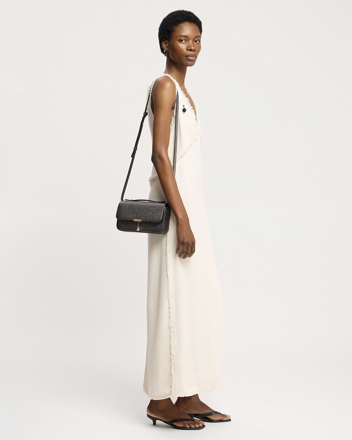 Model in white dress carrying metallic anthracite clutch bag on shoulder