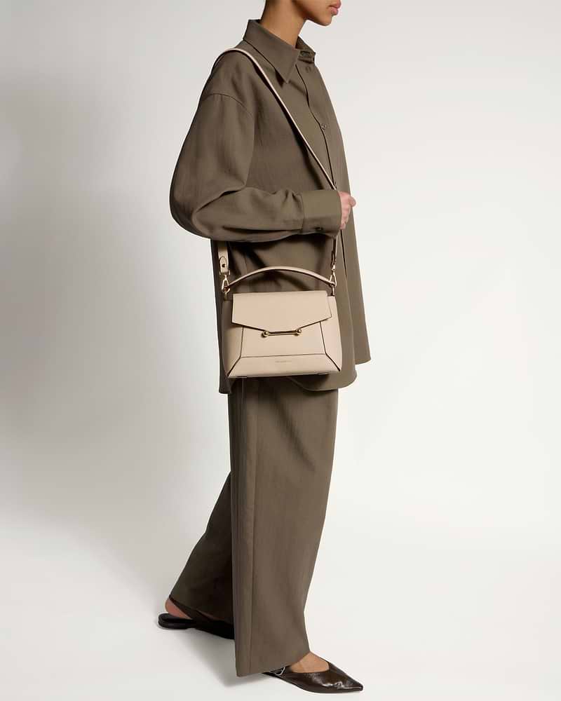 Model wearing oat-coloured mosaic bag with top handle and gold hardware, crossbody.