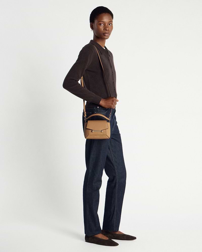 Model wearing a small caramel pebbled leather crossbody bag with top handle and shoulder strap.