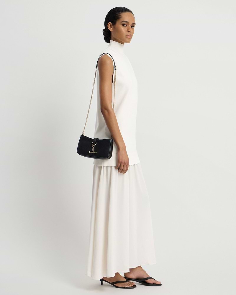 Model in white dress carrying black shoulder bag with gold chain strap and hardware.