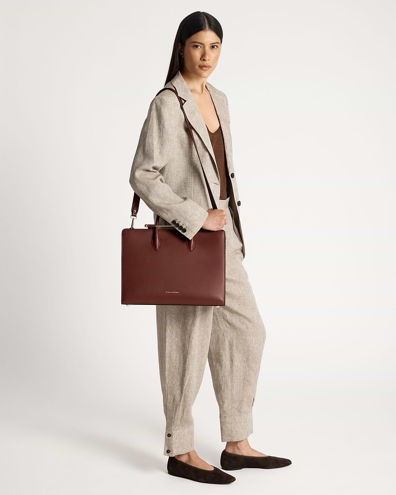 Woman in beige suit holding a walnut Strathberry tote bag by her shoulder.