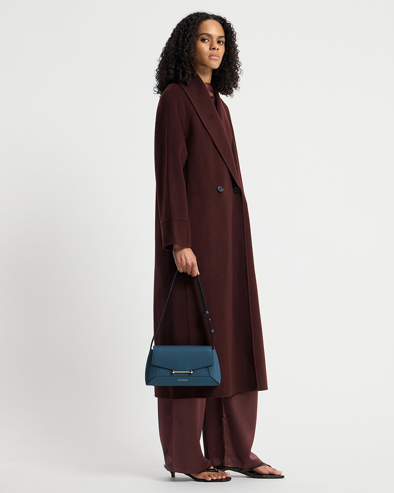 Model wearing long burgundy coat holding Loch Blue Mosaic Shoulder bag by Strathberry.