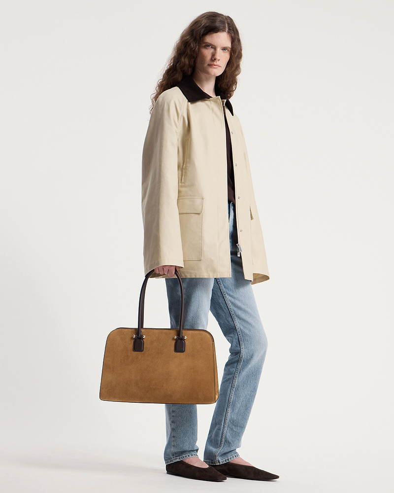 Model carrying toffee suede tote with espresso handles, wearing beige coat and blue jeans.