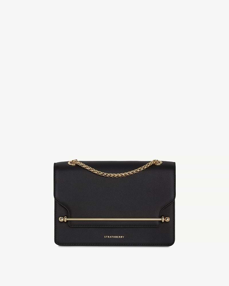 Strathberry east-west bag in black with gold chain handle and metal bar.