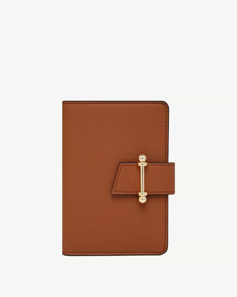 Tan leather passport holder with gold bar clasp on white background