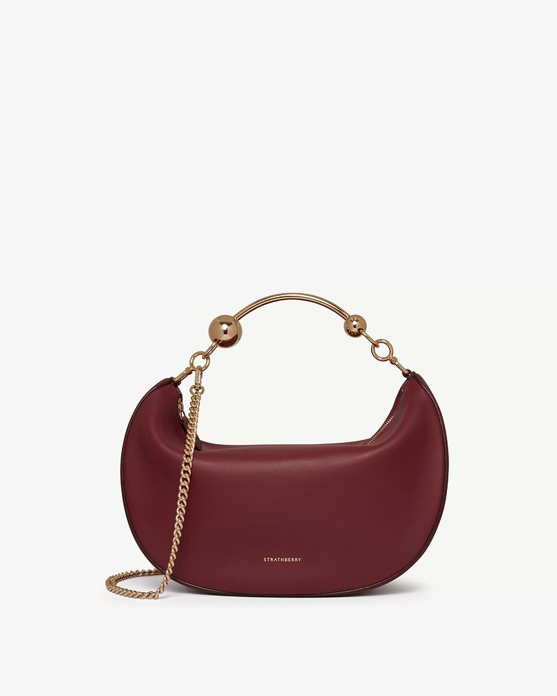 Strathberry Crescent Moon oxblood leather bag with gold metal handle and chain strap.