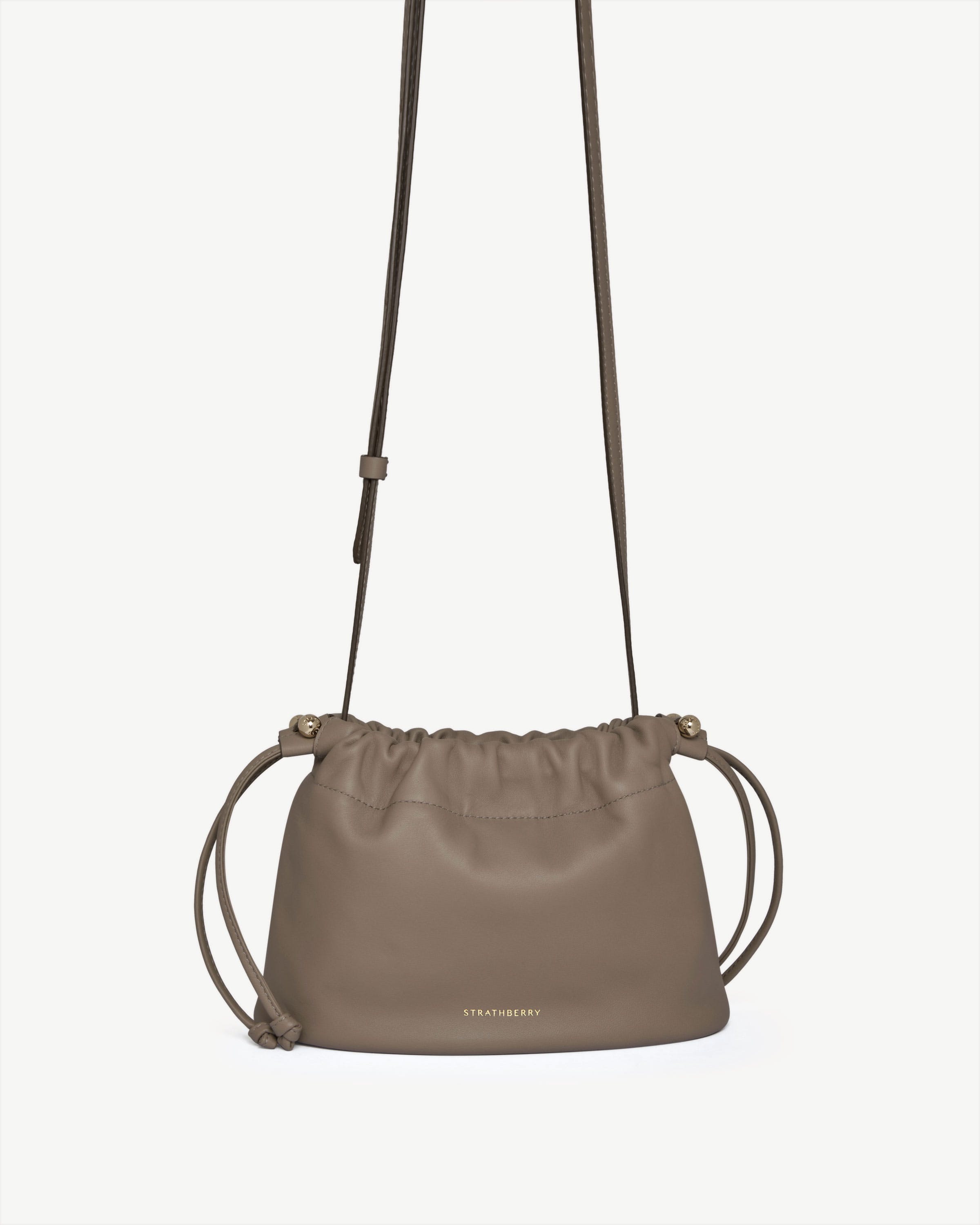 Taupe Strathberry Charlotte drawstring bag with knotted cords, long strap and gold hardware.