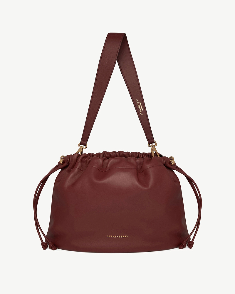 Oxblood Strathberry Charlotte midi drawstring bag with wide shoulder strap.