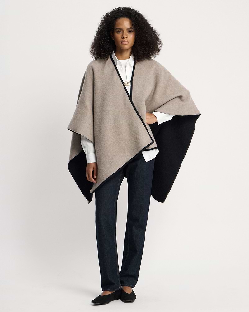 Model wearing otter and black woven cape over white shirt and dark jeans.