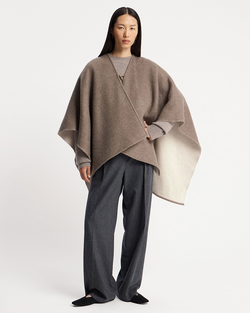 Model wearing a taupe kite woven cape over a grey sweater and trousers.