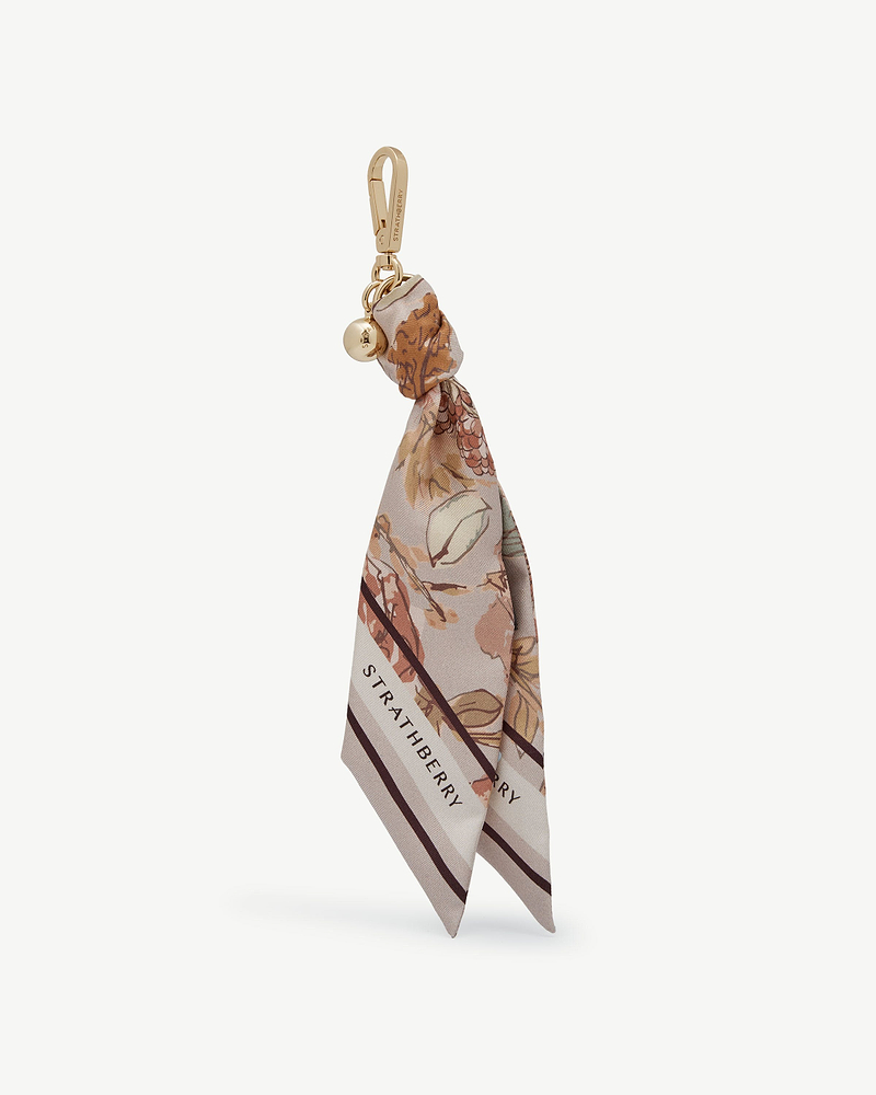 Silk charm with floral print, tied to gold clip, Strathberry logo visible.