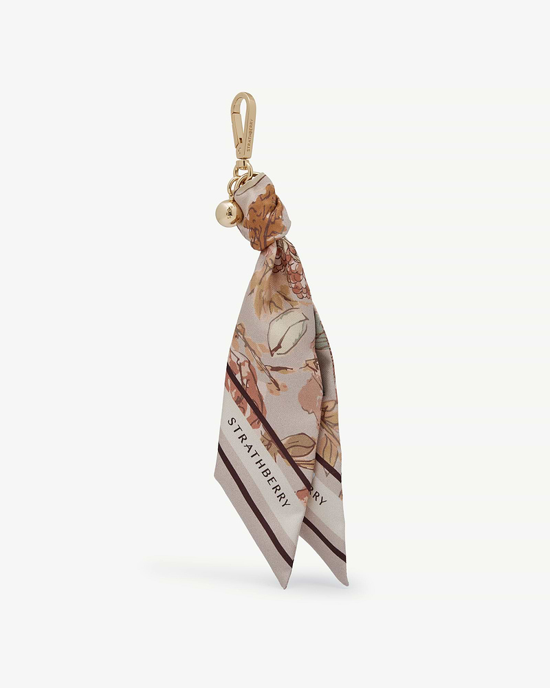Silk charm with floral print, tied to gold clip, Strathberry logo visible.