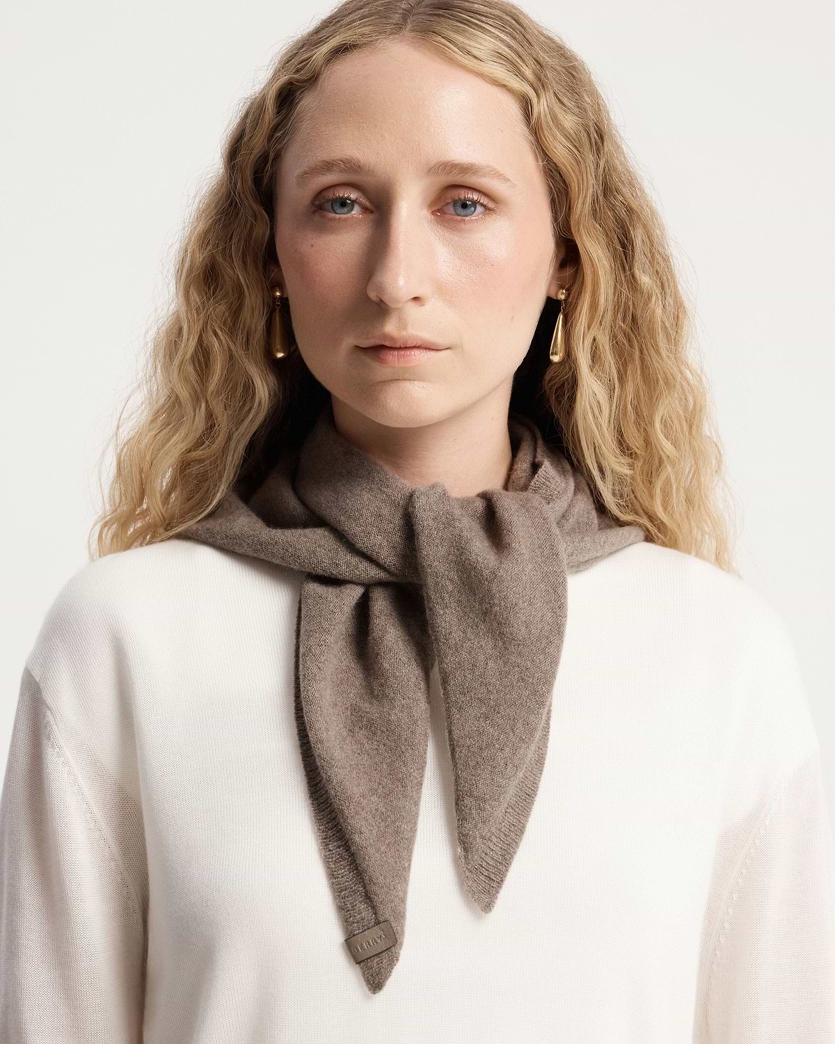 Model wearing pebble cashmere bandana tied at front over white jumper.