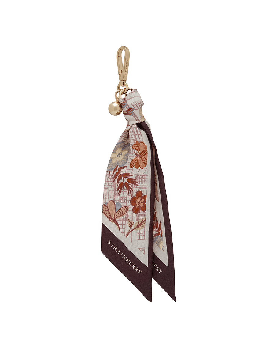 Silk charm with gold clasp and bell, burgundy printed scarf with Strathberry logo.