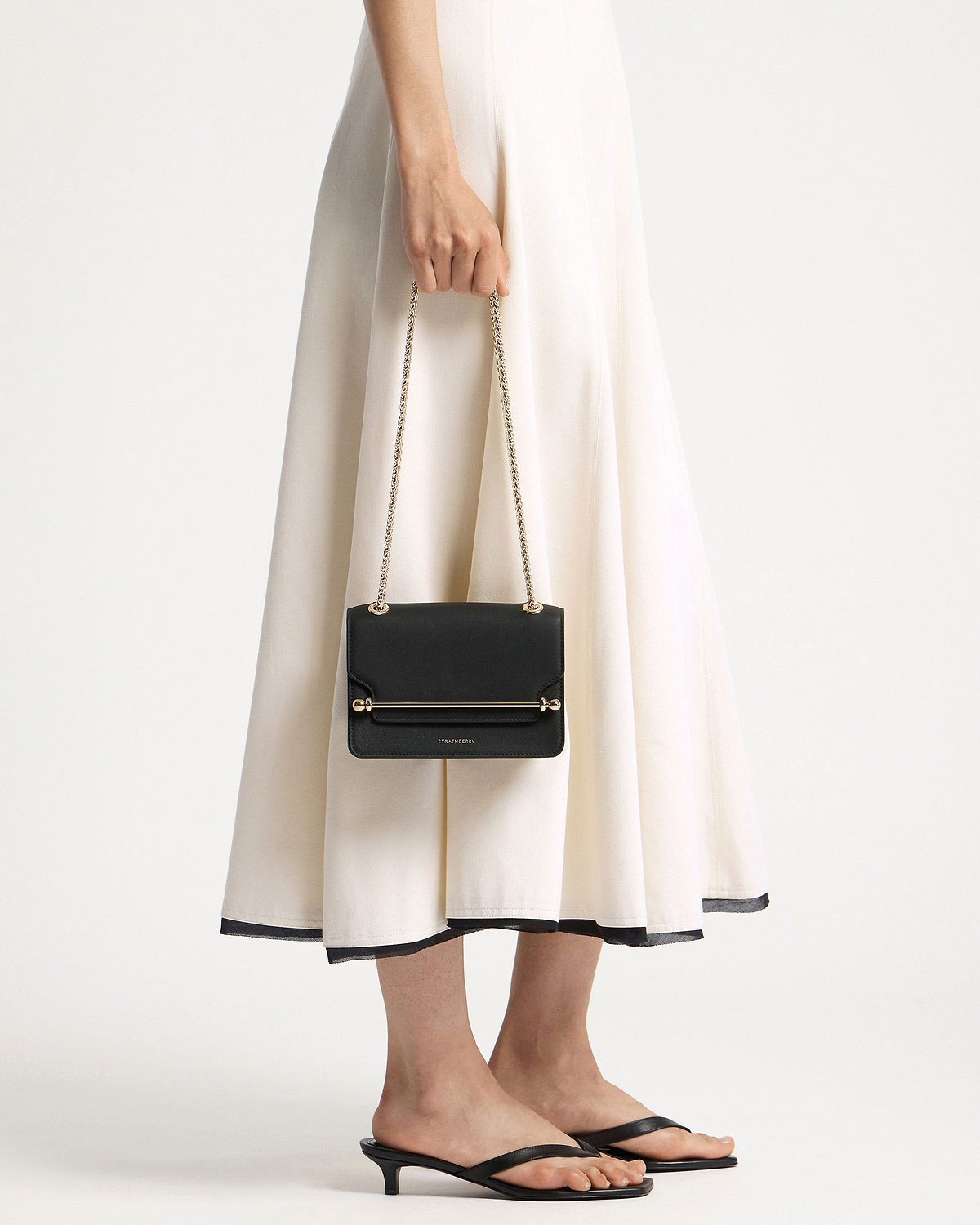 Model holding black Strathberry East/West Mini bag with gold chain strap.