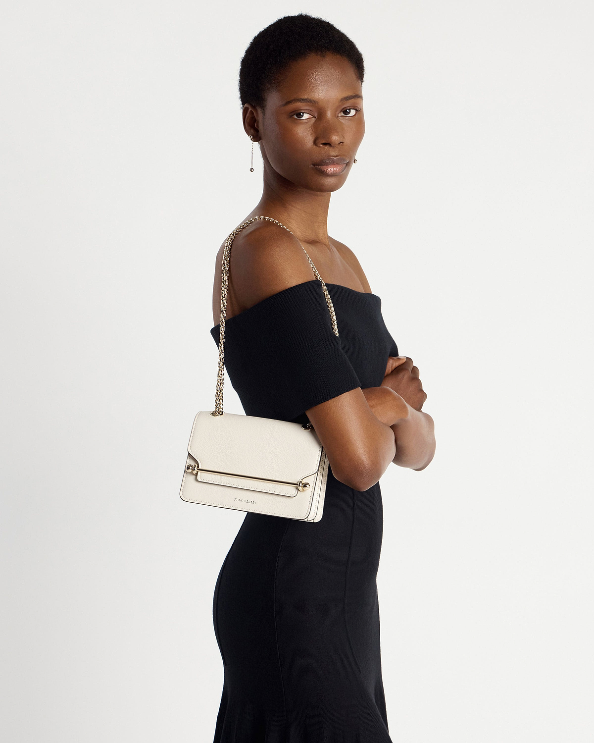 Model wearing black off-shoulder dress with vanilla East/West Mini bag on shoulder.