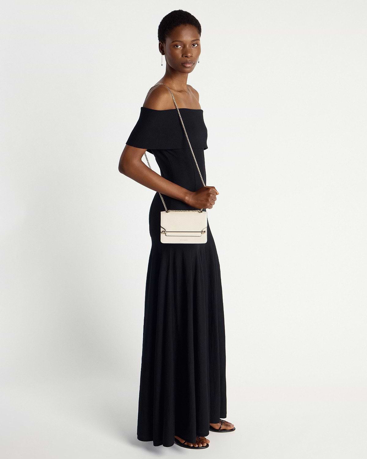 Model in black off-shoulder dress carrying a vanilla Strathberry East/West Mini bag.
