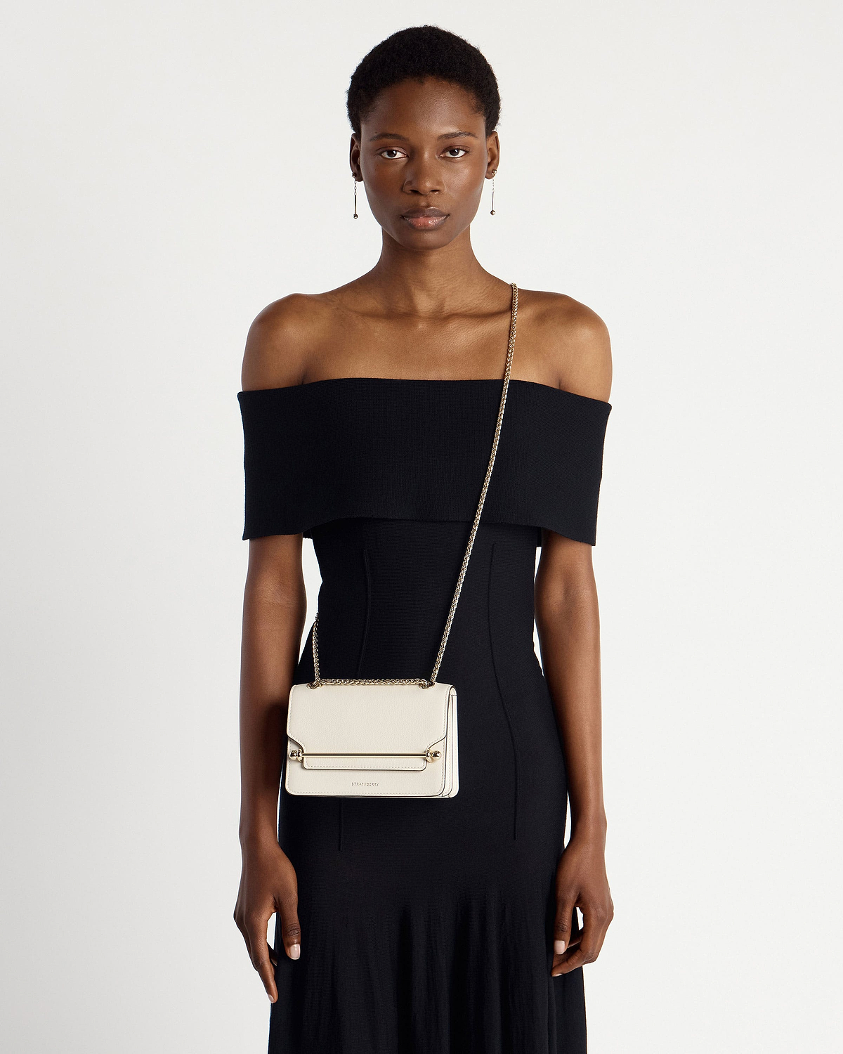 Model wearing a small vanilla crossbody bag with a gold chain strap.