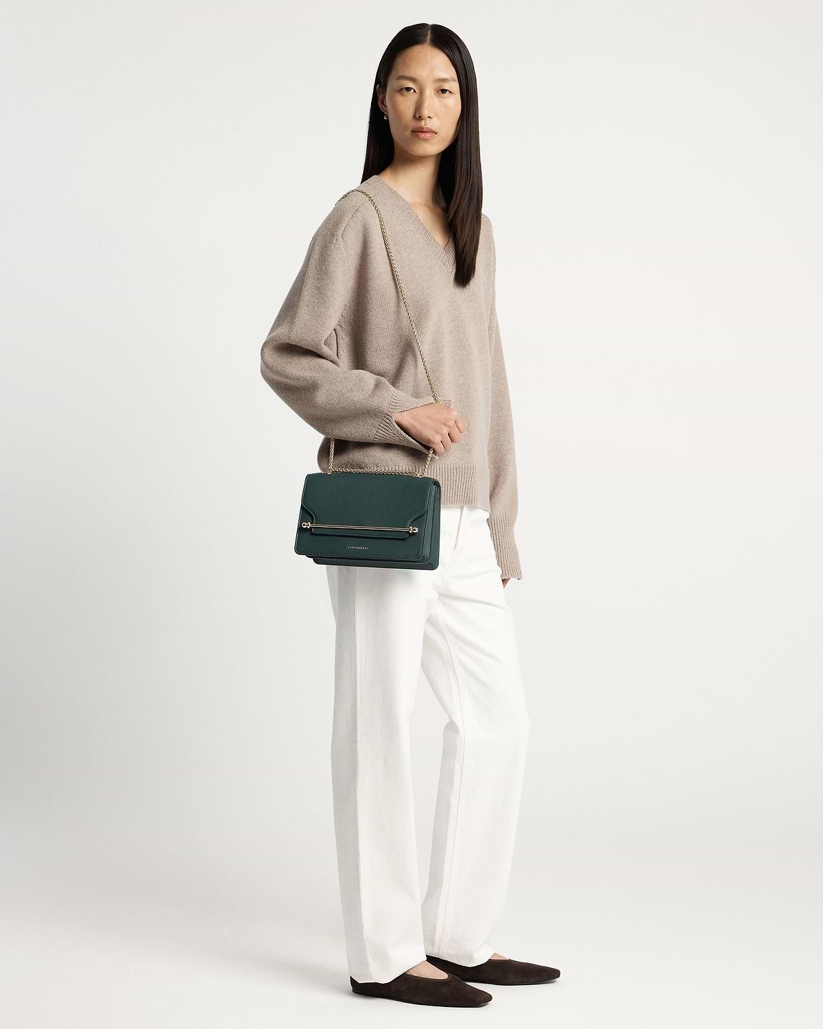 Woman wearing beige jumper and white trousers carrying bottle green east/west bag.