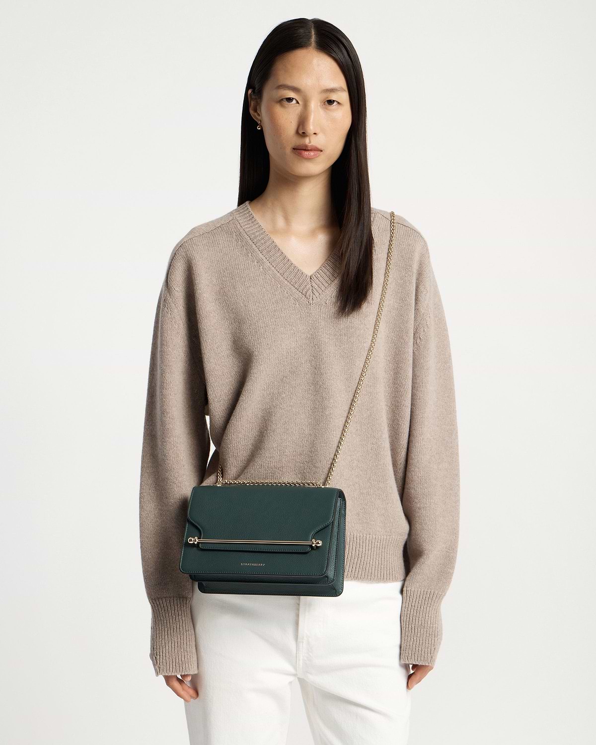 Model wearing bottle-green east/west leather cross-body bag with gold chain strap.