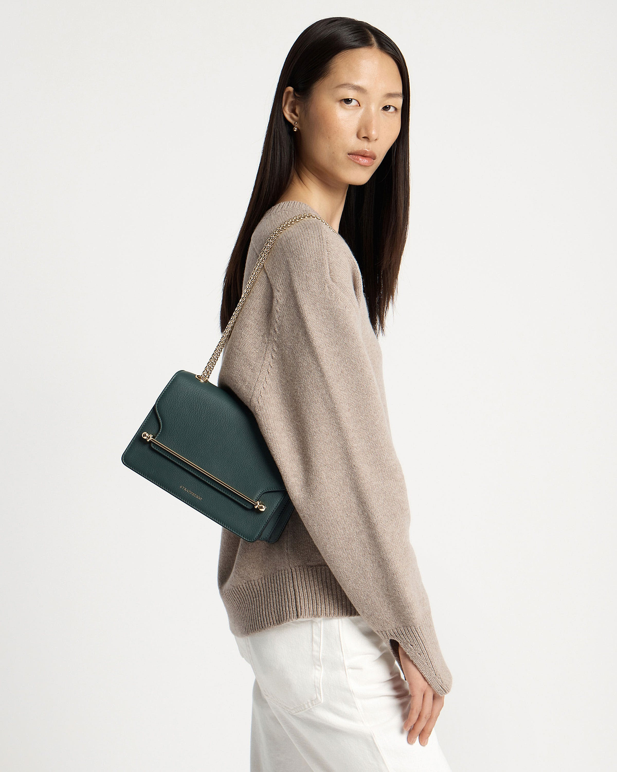 Model wearing bottle green east/west shoulder bag with gold chain strap.