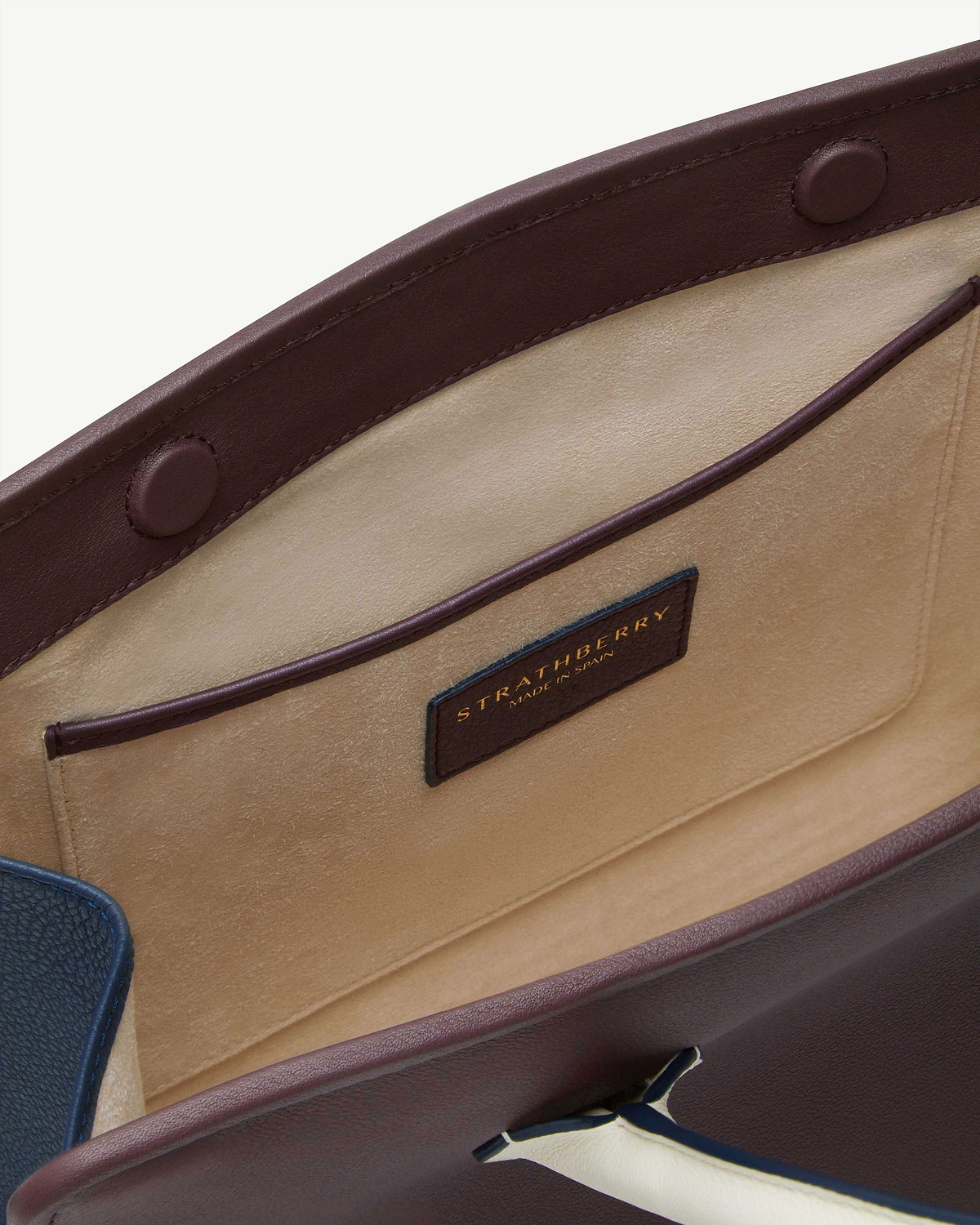 Interior of burgundy-trimmed midi tote showing beige suede pocket and Strathberry label.