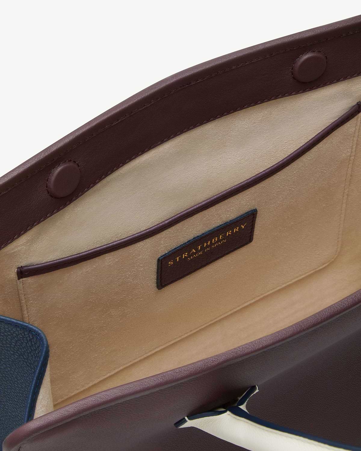 Interior of burgundy-trimmed midi tote showing beige suede pocket and Strathberry label.